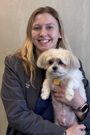 Andi Blonde woman smiling and holding a white dog
