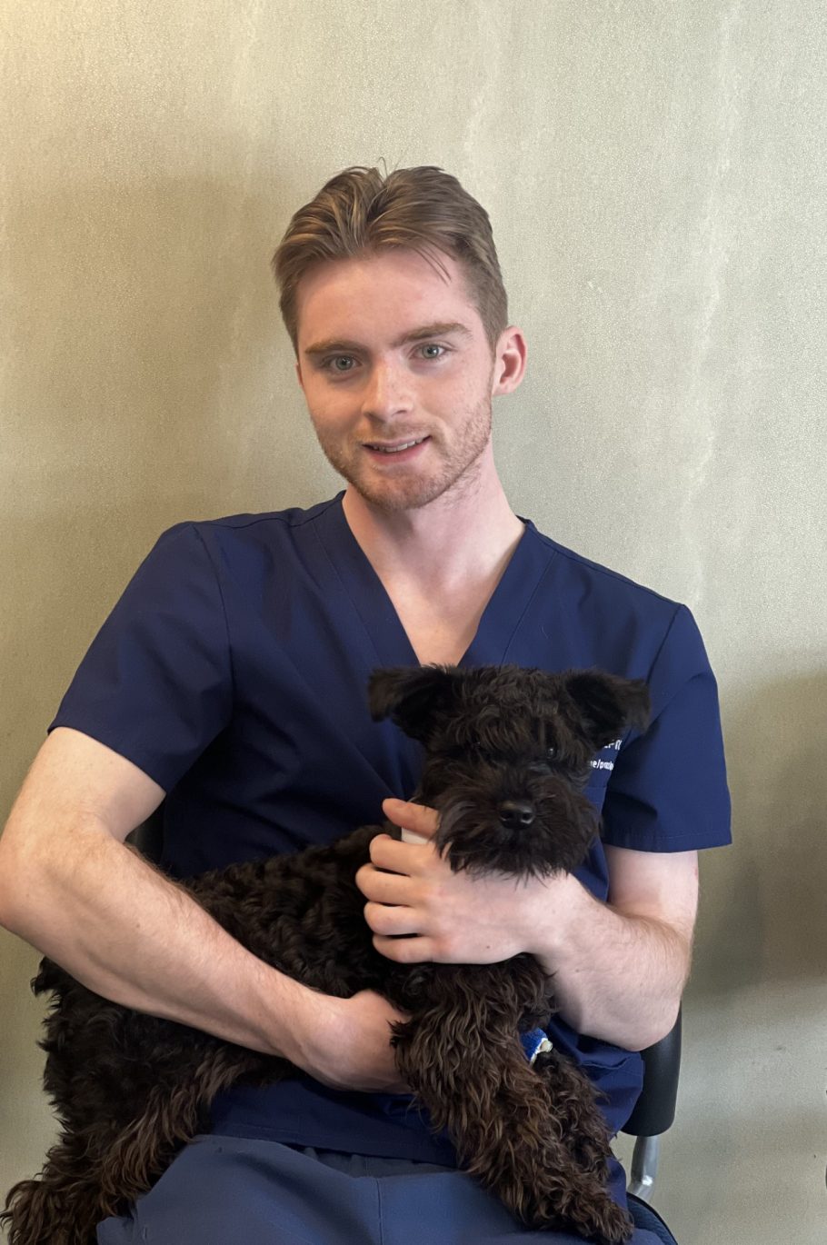 Brendan in the office wearing scrubs holding a dog